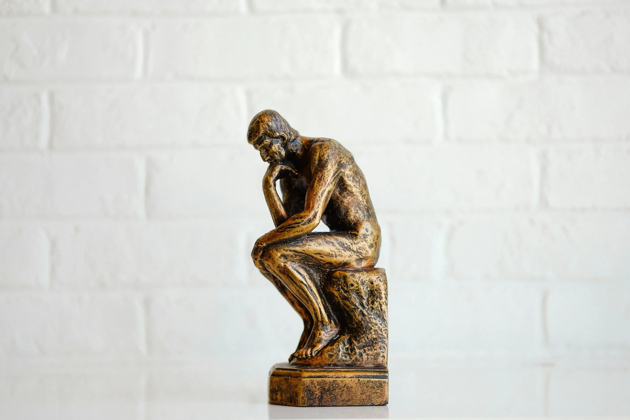 Bronze statue with guy kneeling with fist to face signifying thought